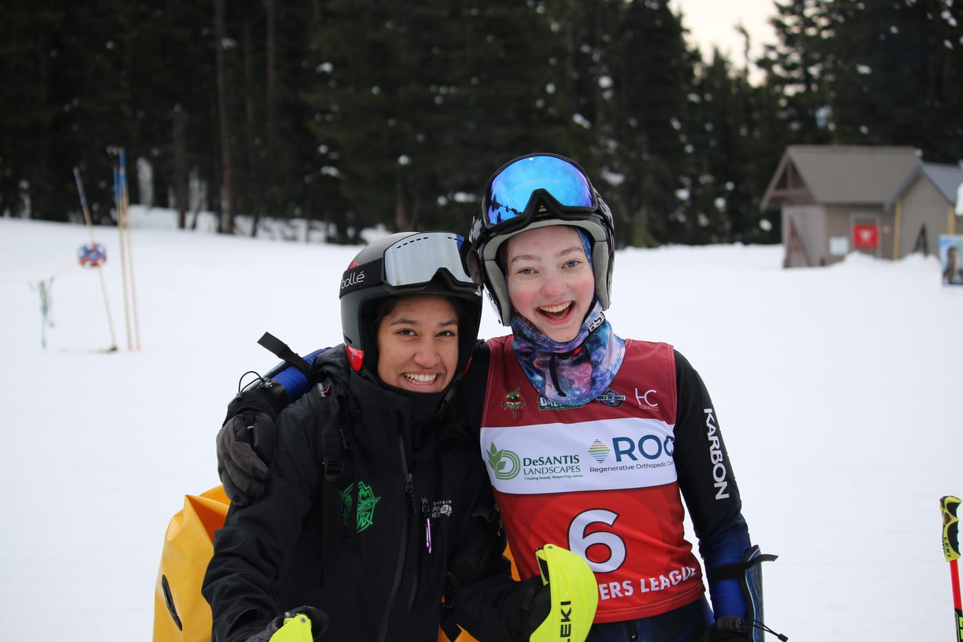 Two racers grinning with their arms around each other in the finish area, one still wearing a Three Rivers League bib