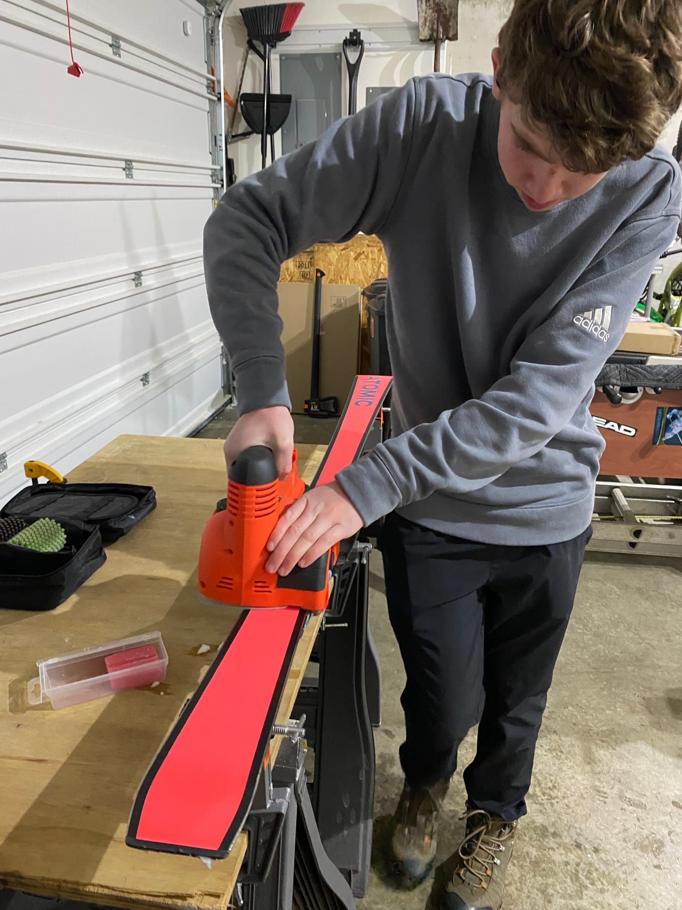 An athlete running a waxing iron down a race ski on a bench in a garage